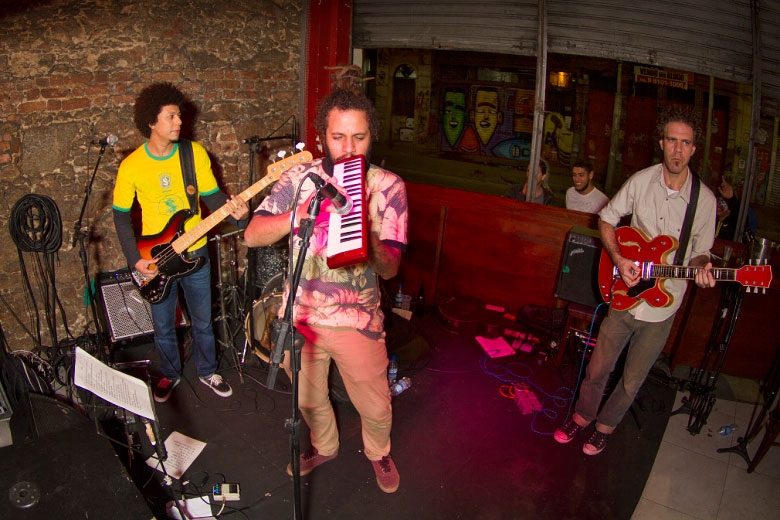 Depois do jogo Brasil x Camarões pela Copa do Mundo, a banda Muzamba deu início a noite tocando os clássicos do dub e do reggae. Na foto Angelo B no baixo, Bruno Pederneiras na guitarra e o vocalista André Machado na escaleta. Fotos: Radio Layback